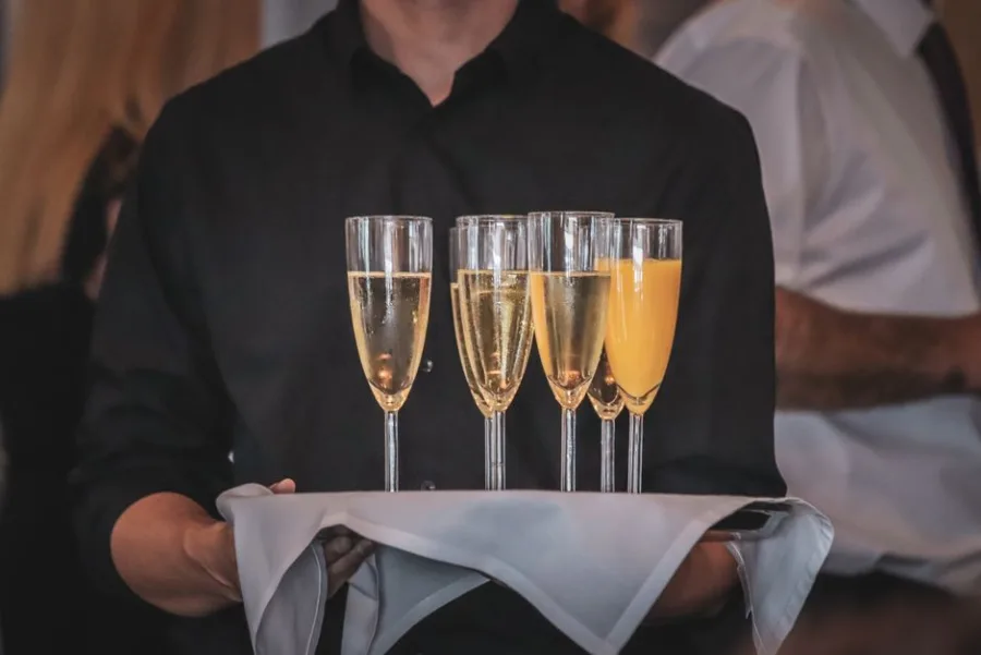 Felszolgáló tálcán pezsgős és üdítős poharakat visz
